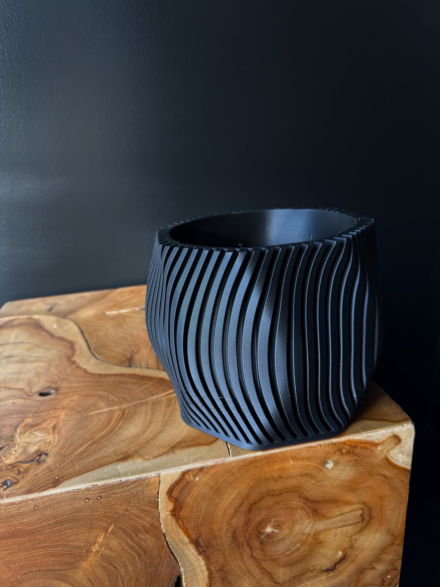 Two 3D printed pots, one white and one black, with a removable drip tray, placed on a wooden surface against a dark background.