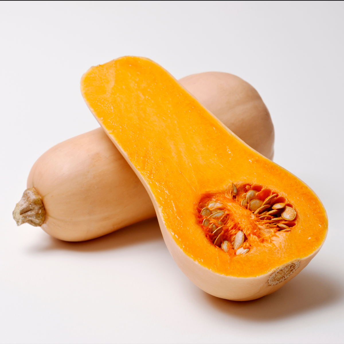 two butterbaby butternut squash one whole and one half displaying its bright orange inside with a pocket of seeds against a white background