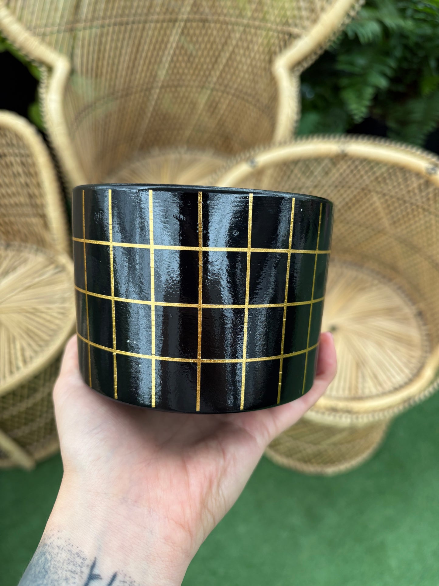 hand holding Cyrus Gold and Black Pot in front of blurred background of wicker chairs