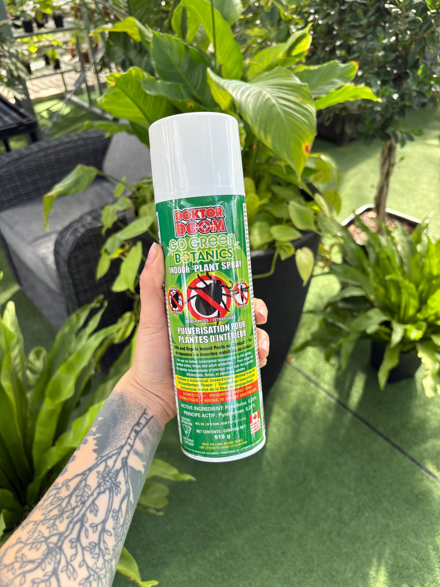Hand holding a green and white spray bottle of Dr. Doom Go Green Botanics Plant Spray with plant in background