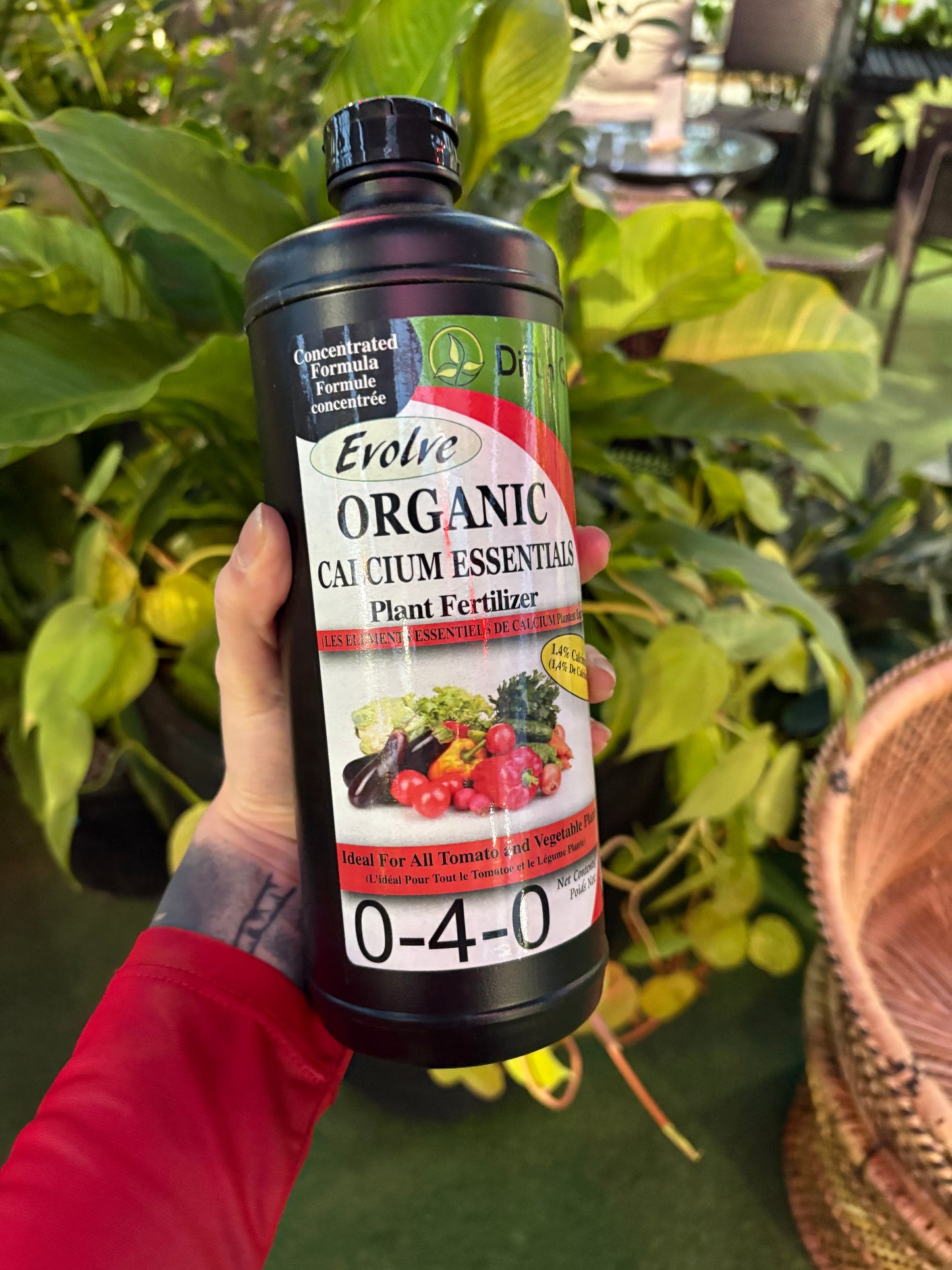 Hand holding a bottle of Organic Calcium Essential Plant Food with plants in the background