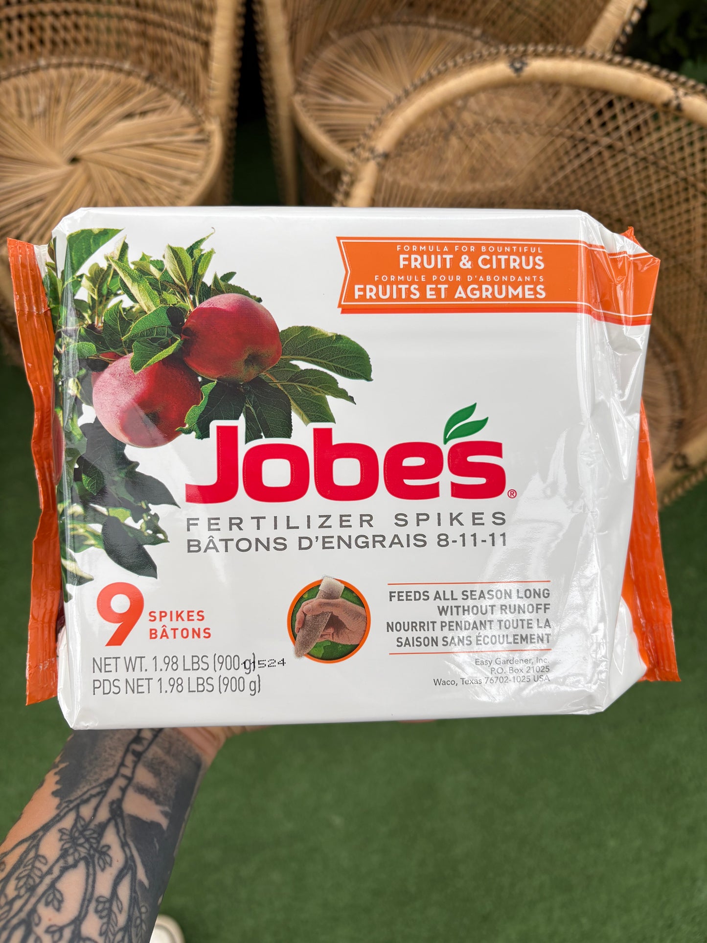 hand holding a package of Fruit & Citrus Fertilizer Spikes in front of wicker chairs