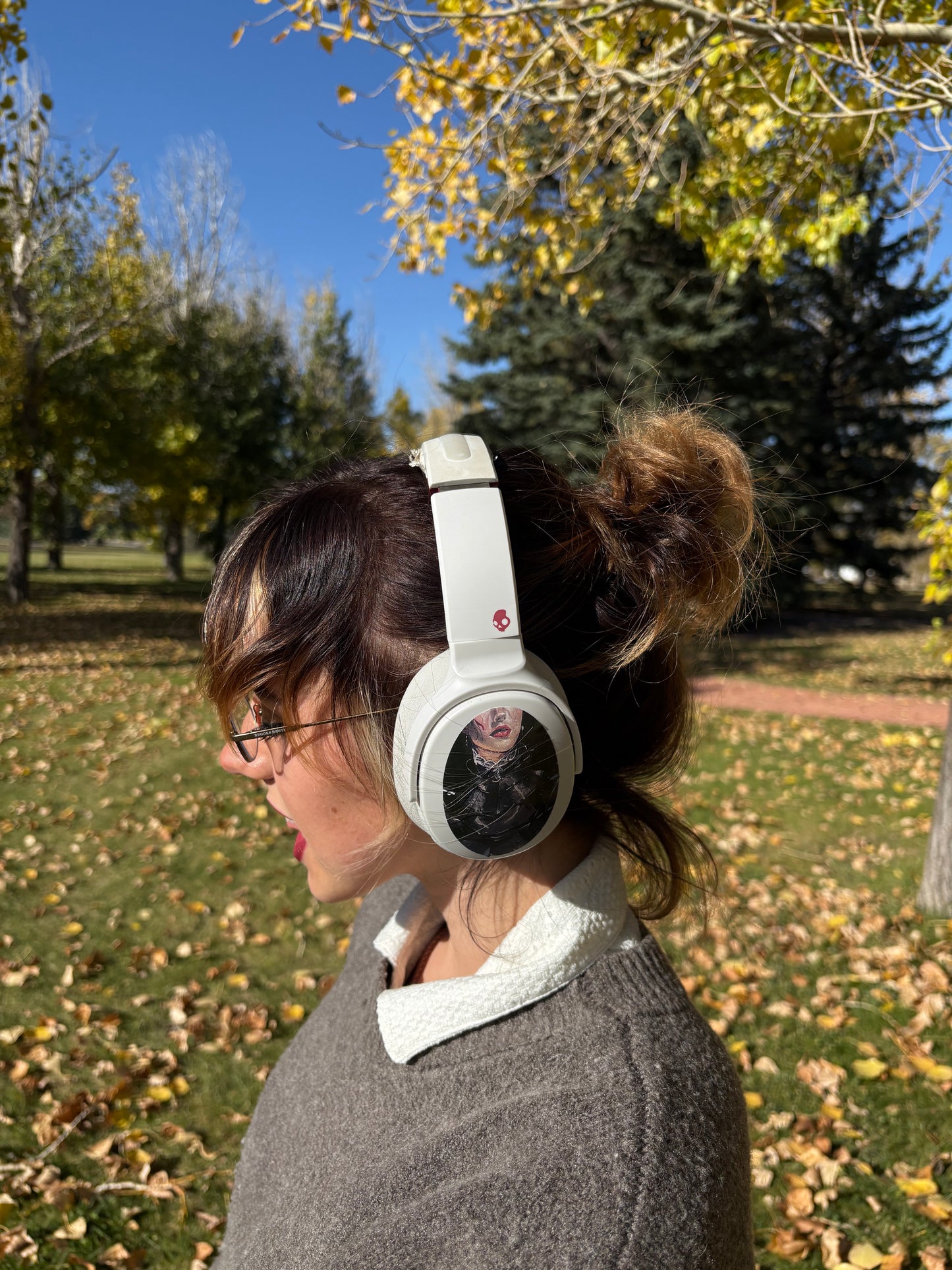 Person wearing white headphones outdoors with trees and grass in the background