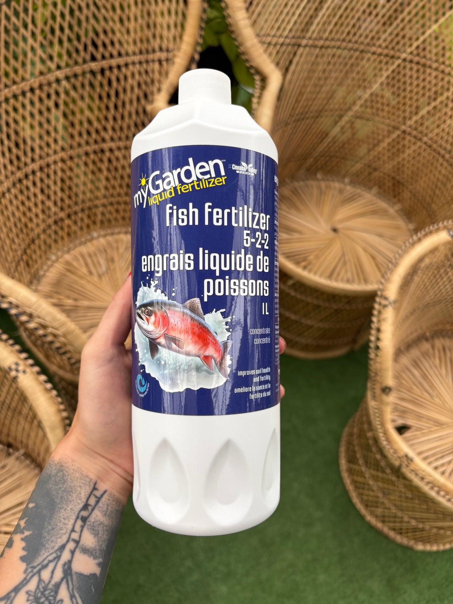 Hand holding a bottle of fish fertilizer with wicker chairs in the background