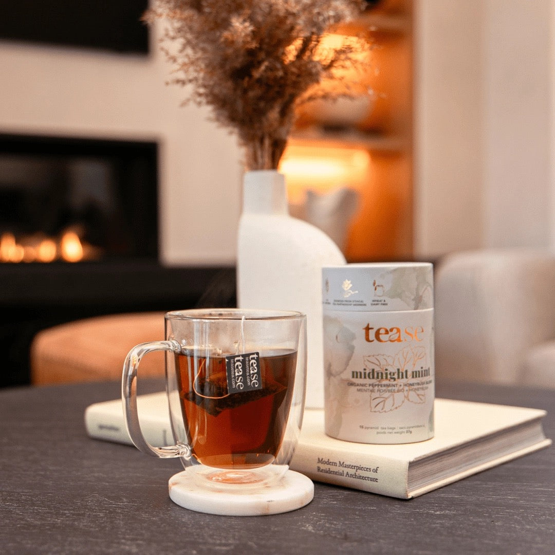 Tea cup with a package of 'tease' tea on a table in a cozy room with a fireplace.