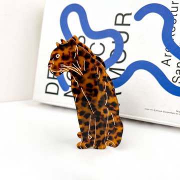 Cheetah shaped an coloured hair blip resting on white surface with book in background