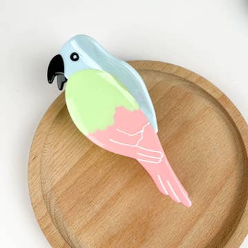 pastel blue yellow and pink parrot hair clip resting on wooden disk with white background