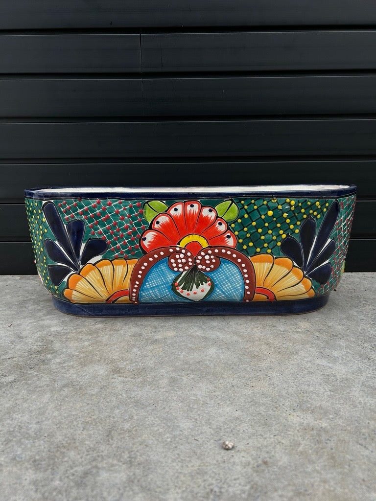 colourful canoe shaped planter resting on concrete floor with black slate background