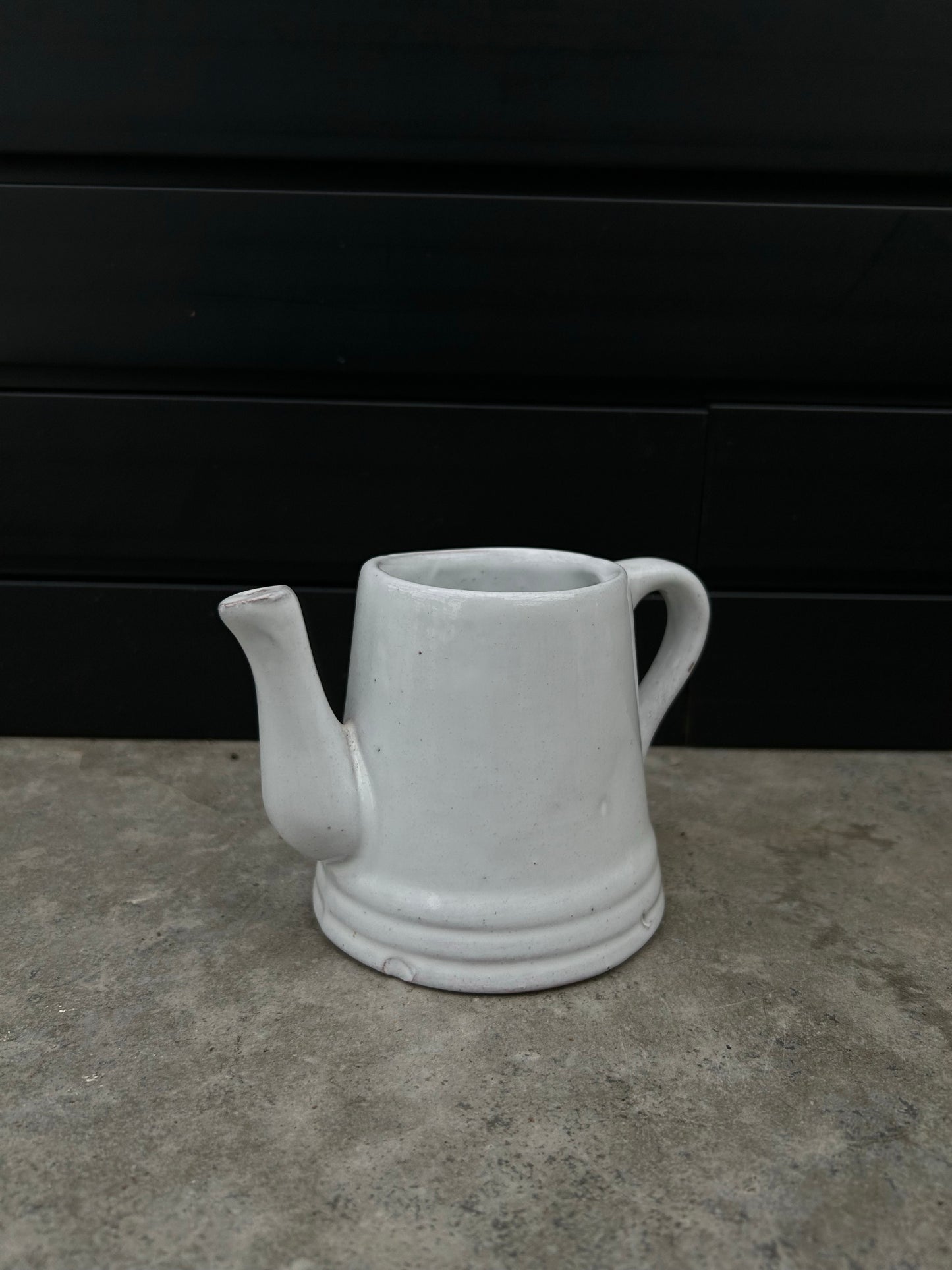 light grey ceramic pot shaped like watering can on concrete floor with black background