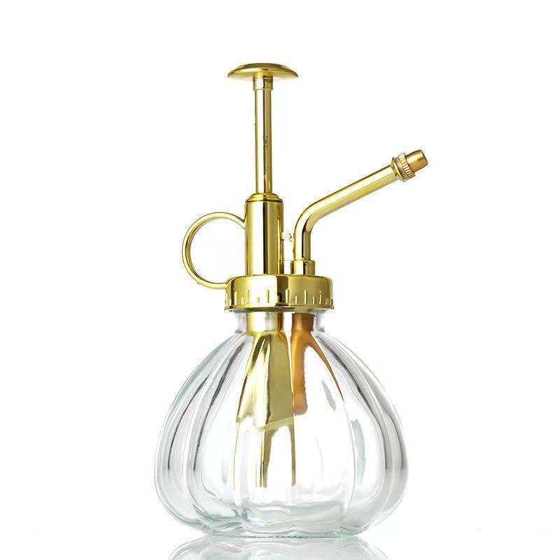 A stylish glass watering spray bottle with a gold-colored metal pump and spout.
