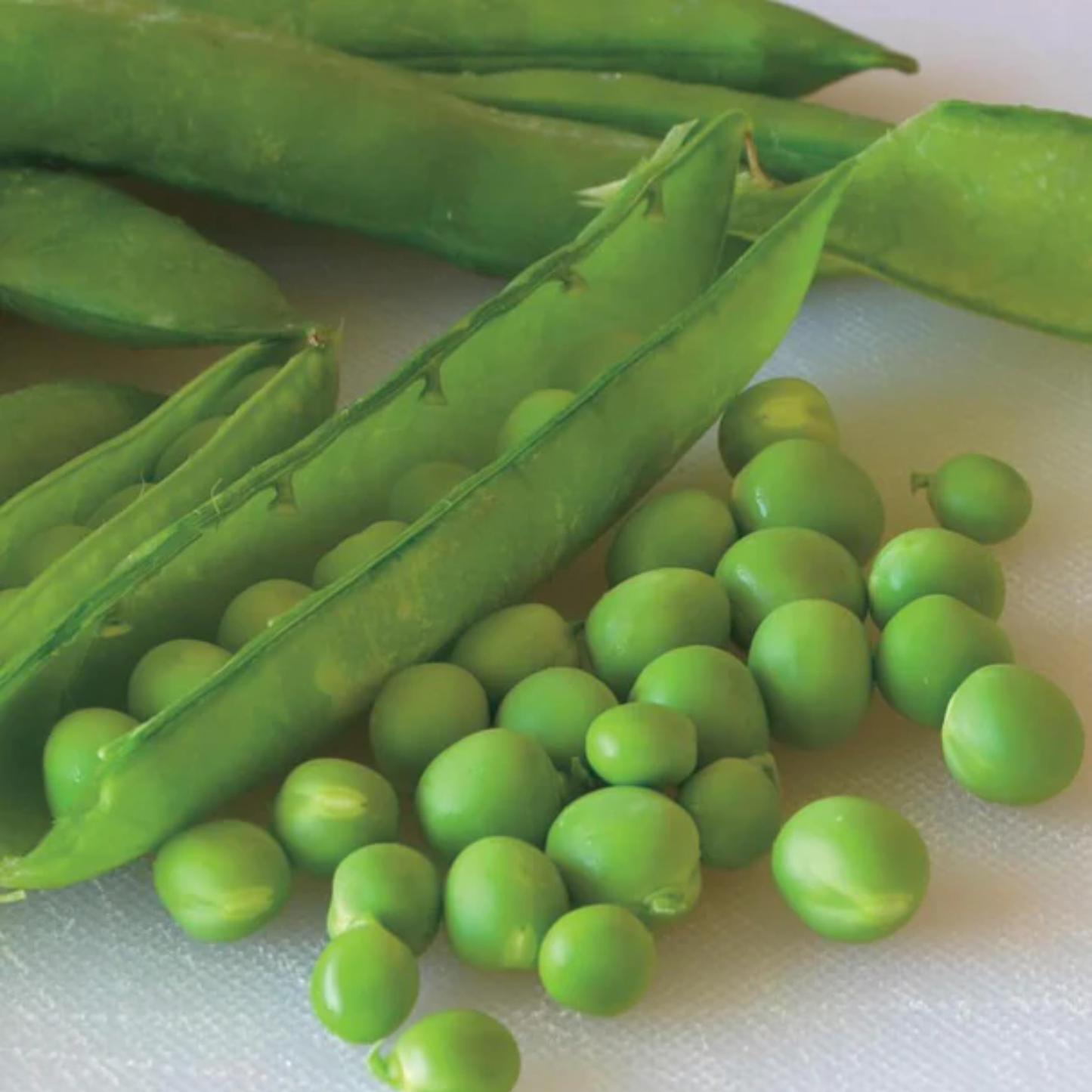 many loose green peas next to green pods of green arrow peas