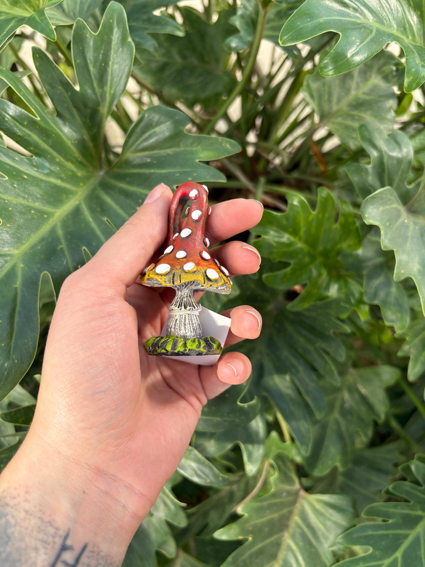 Hand holding a small mini toadstool figurine with a plant in the background