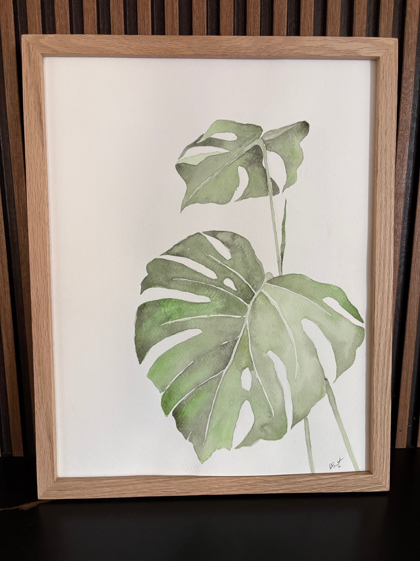 Framed artwork of green monstera leaves on a white background