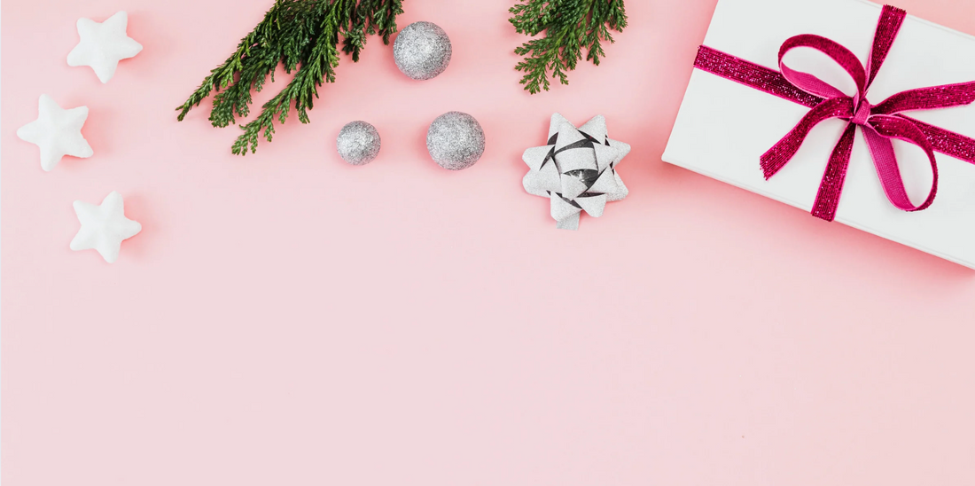 a wrapped present surrounded by some greenery and ornaments or a pink background