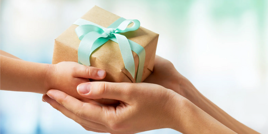 two sets of hands holding a paper wrapped gift with a teal bow