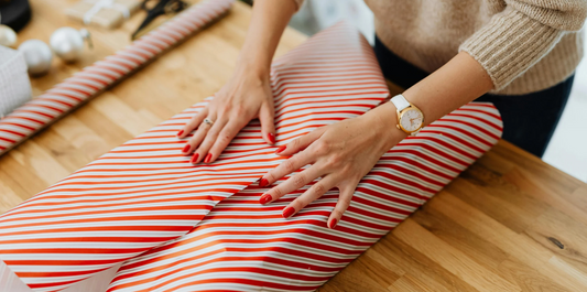 hands wrapping a Christmas gift in white and res wrapping paper