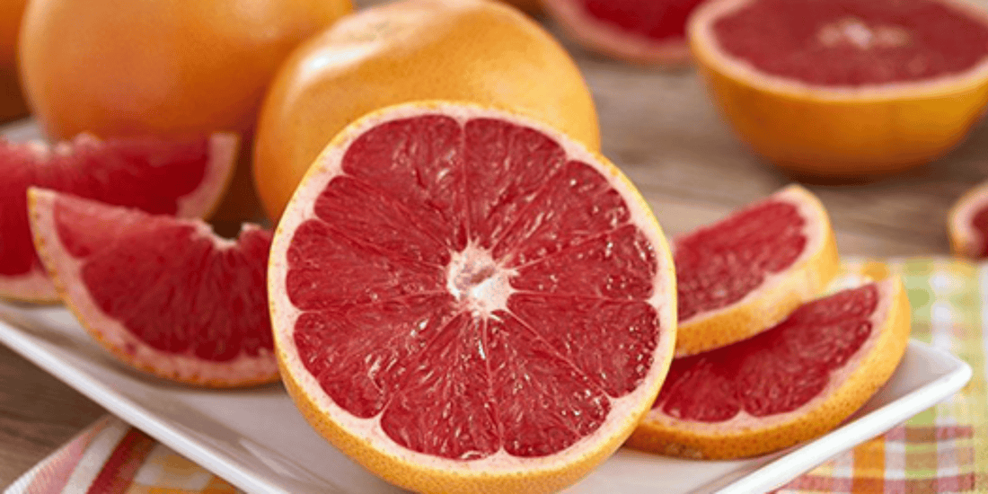 many ruby red grapefruits, some whole, some cut in half, and some in slices resting on a table