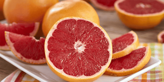 many ruby red grapefruits, some whole, some cut in half, and some in slices resting on a table