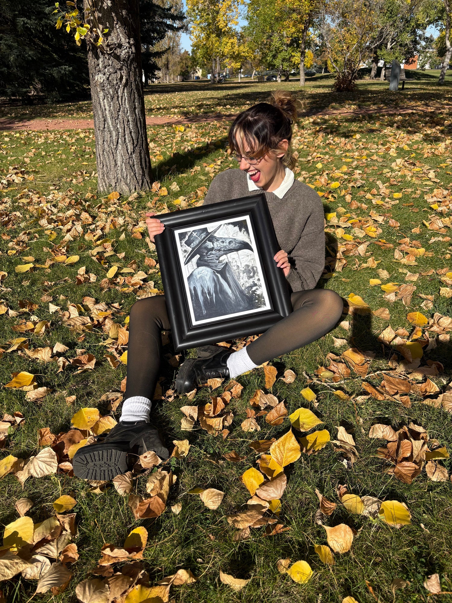 person sitting on the ground outdoors holding a framed print of the plague doctor by Laura Alexander