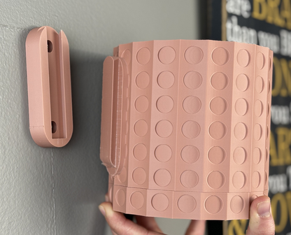 a pink wall mounted pot with removable drip tray showing how it can be removed on and off the wall, on a light grey wall