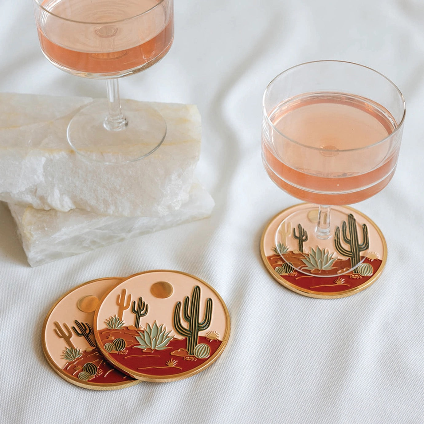 Coasters with cactus design on a white surface with glasses of pink drink.