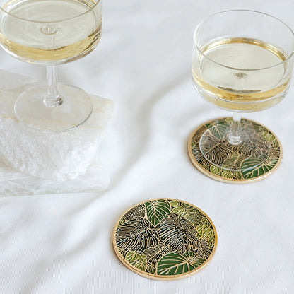 Two glasses of white wine on decorative coasters with leaf patterns on a white surface.