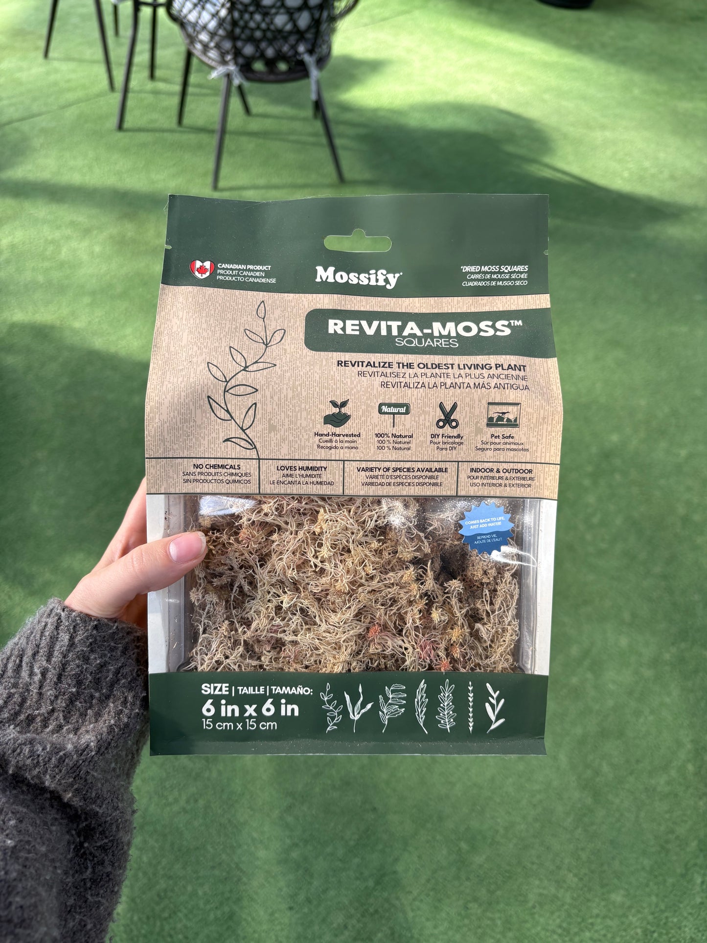 Hand holding a package of Revita-Moss on a green surface