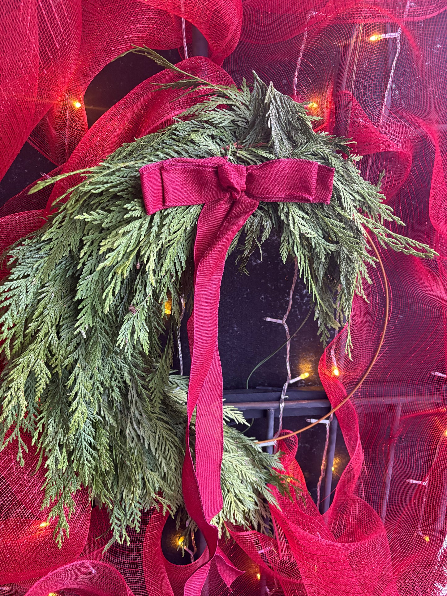 Green Cedar Halfmoon 18" wreath with a red ribbon on a red mesh background with lights