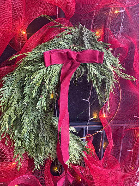Green Cedar Halfmoon 18" wreath with a red ribbon on a red mesh background with lights