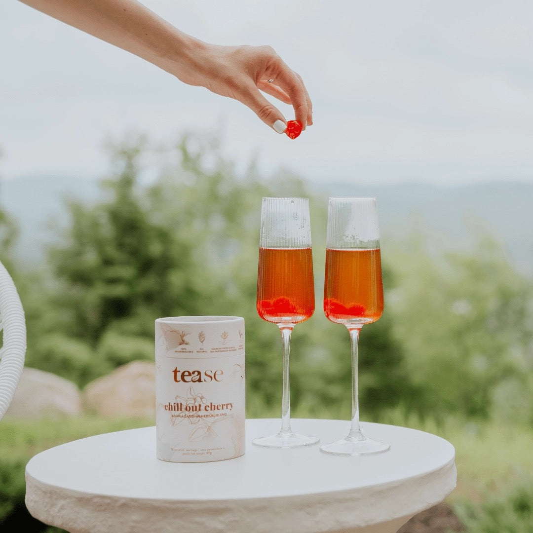 Two glasses of cherry-laced tea with a canister labeled 'tease' on a table outdoors.