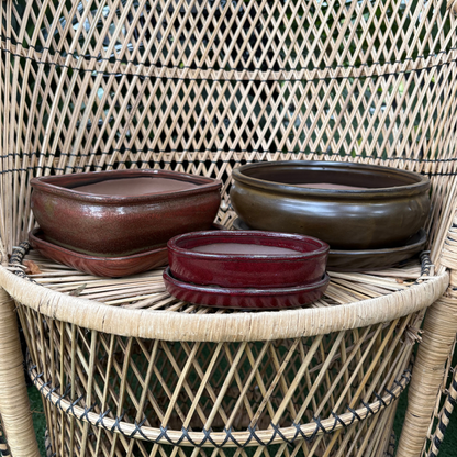 three Chinese glazed ceramic bonsai pots of different sizes and colours all beside each other resting on a wicker chair