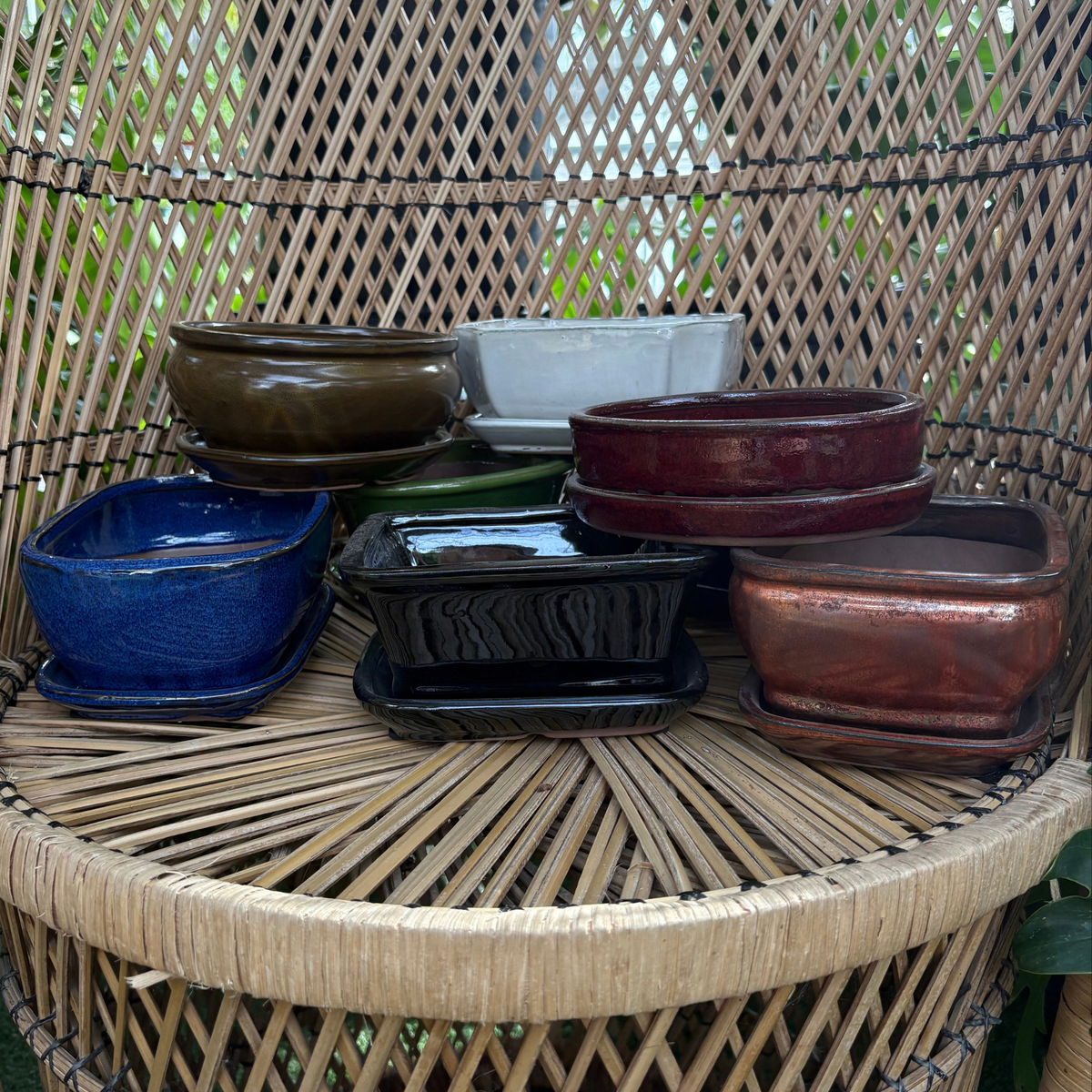 many Chinese glazed ceramic bonsai pots of many different colours and shapes stacked on top of each other resting on a wicker chair
