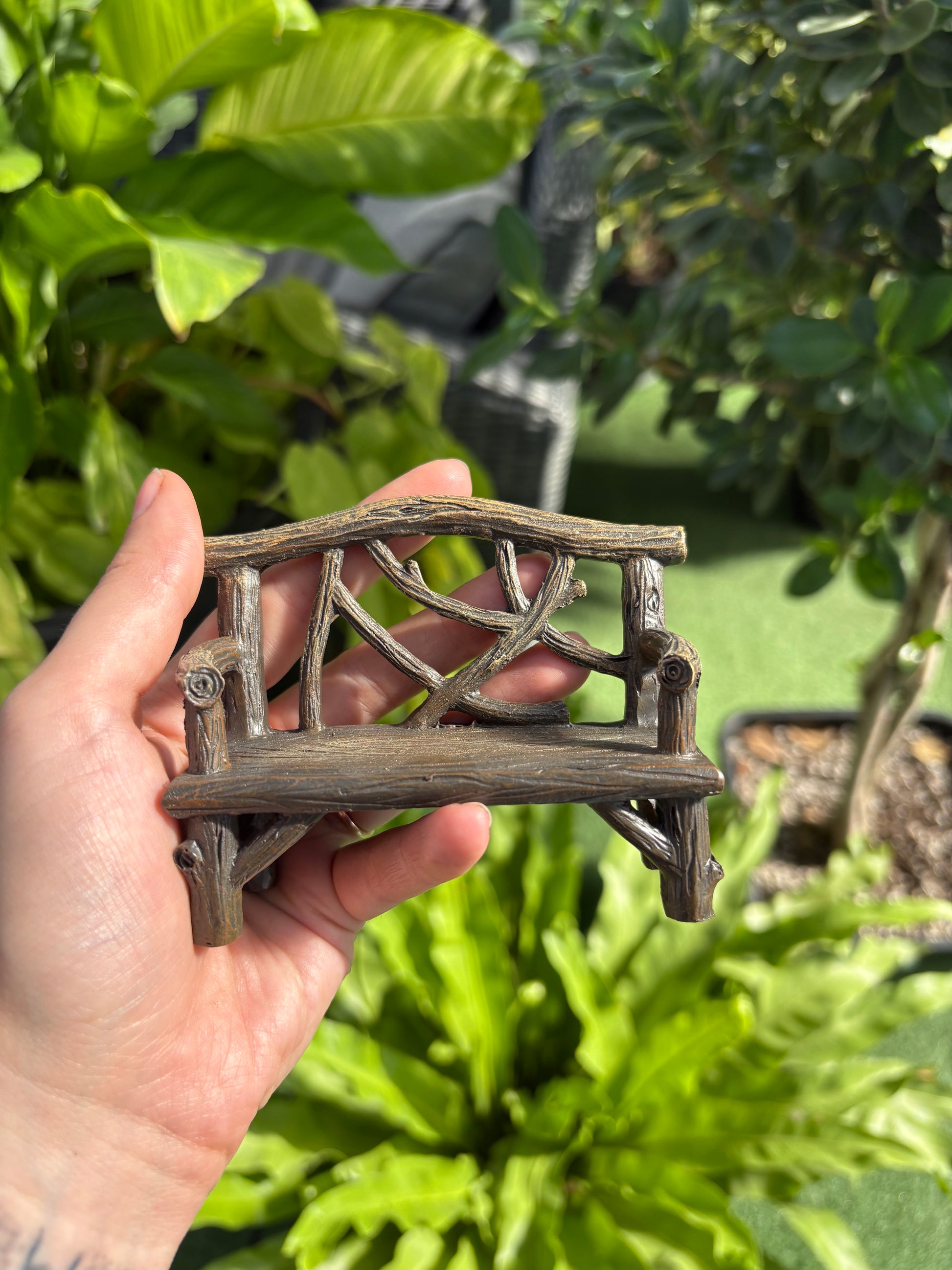hand holding a small fairy garden bench in a greenhouse setting
