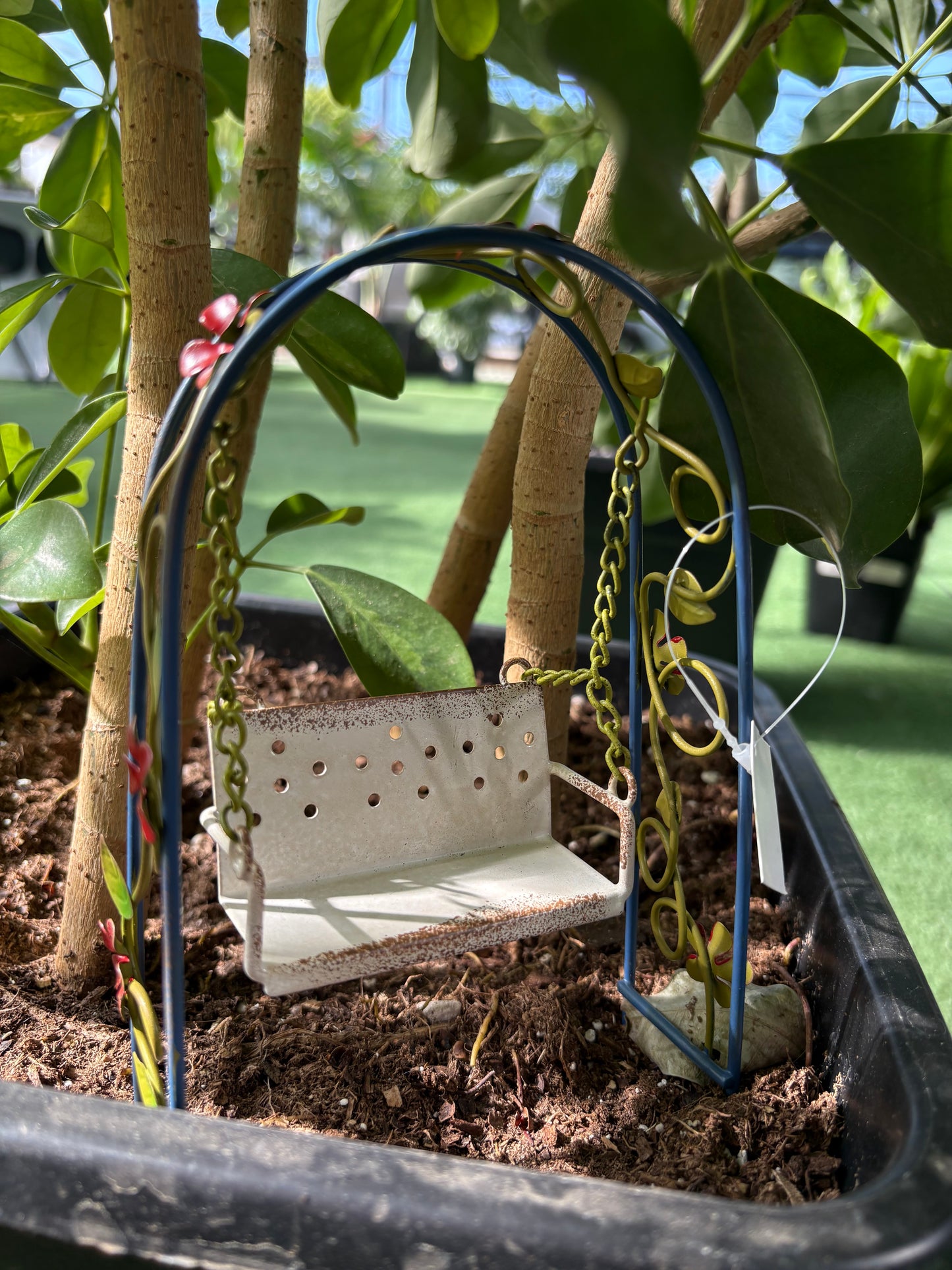 metal fairy swing. fairy garden swing in a pot surrounded by greenery