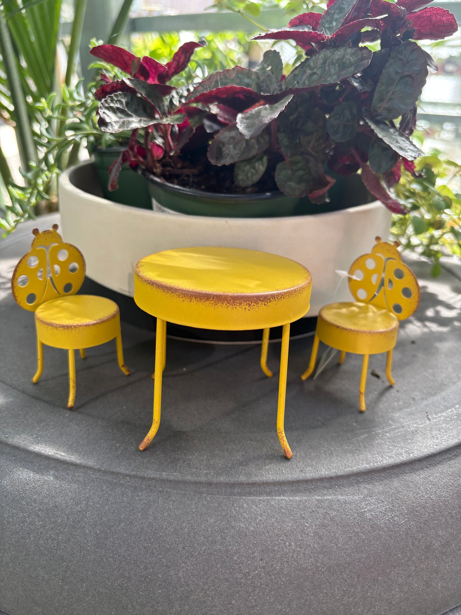 yellow metal Fairy Table and Chairs Set on a grey surface with plants in the background