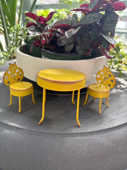 yellow metal Fairy Table and Chairs Set on a grey surface with plants in the background