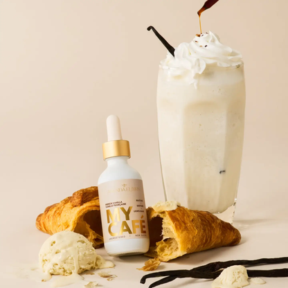 a white proper bottle with a tan label that says my cafe French vanilla with the bottle resting on a croissant with a white French vanilla iced beverage behind it and aa cream coloured white background