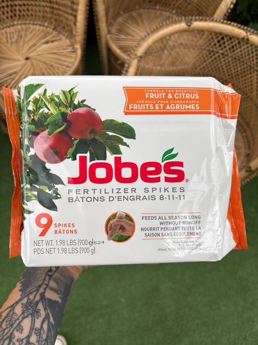 hand holding a package of Fruit & Citrus Fertilizer Spikes in front of wicker chairs