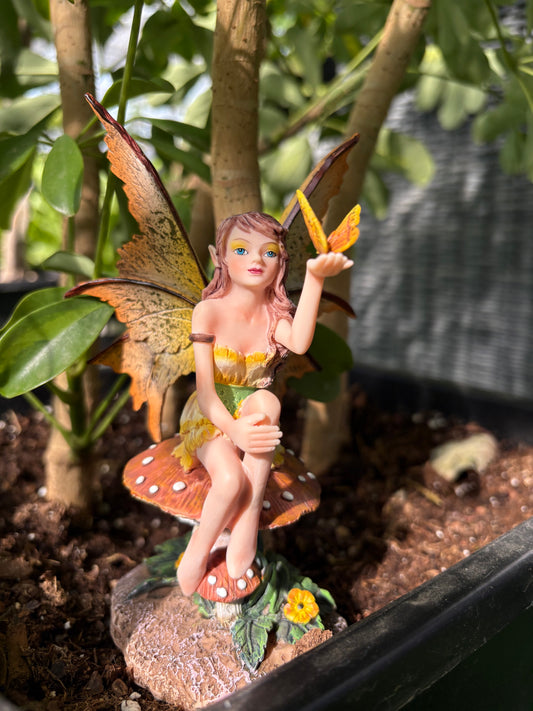 Golden Butterfly Fairy figurine sitting on a mushroom with a natural background