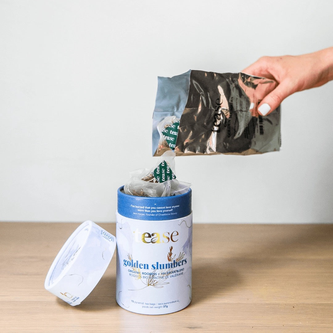 hand pouring bag of tease golden slumber tea refills into container on wooden surface