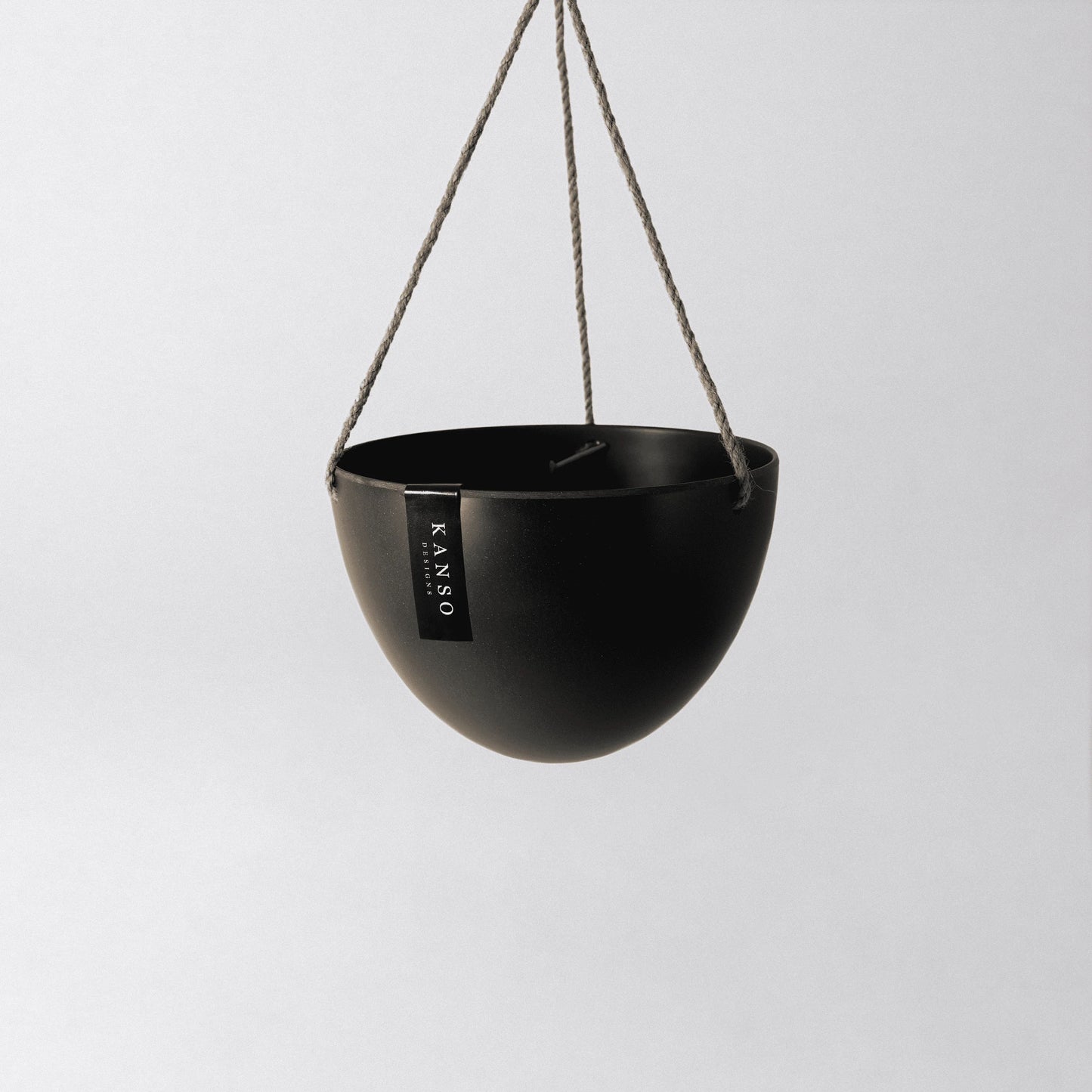 Black hanging planter with 'KANSO'  designs branding on a light gray background
