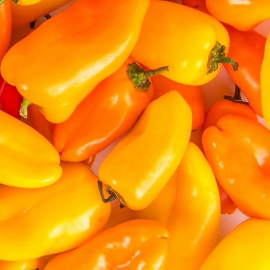 a pile of bright yellow and orange kitchen minis fresh bites yellow peppers with green stems on a white surface