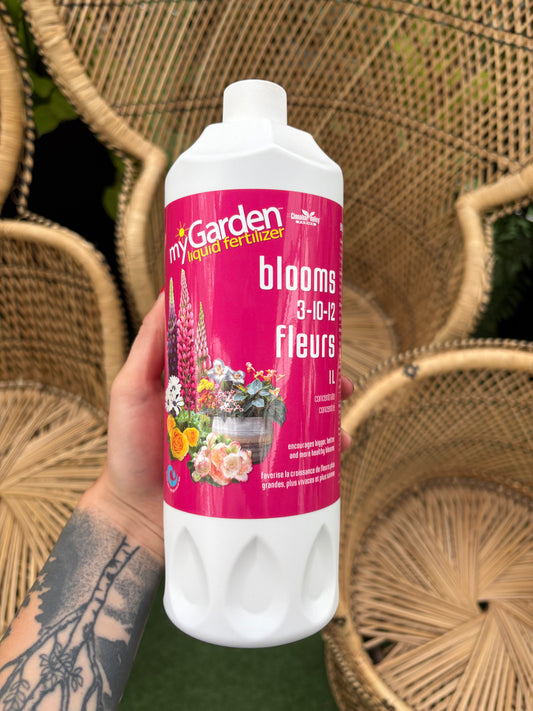 Hand holding a bottle of flower fertilizer with a blurred background