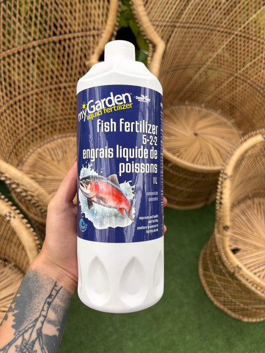 Hand holding a bottle of fish fertilizer with wicker chairs in the background
