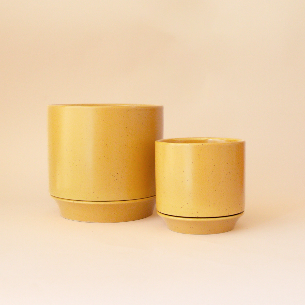 two yellow Parker planters with trivets and the planters are different sizes with a pale yellow background