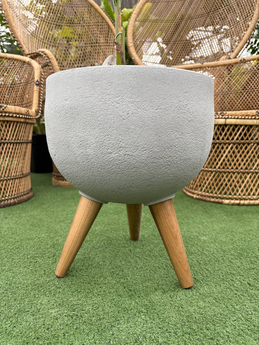 Rustic Round Planter with Wooden Legs on grass like surface with wicker chairs in background