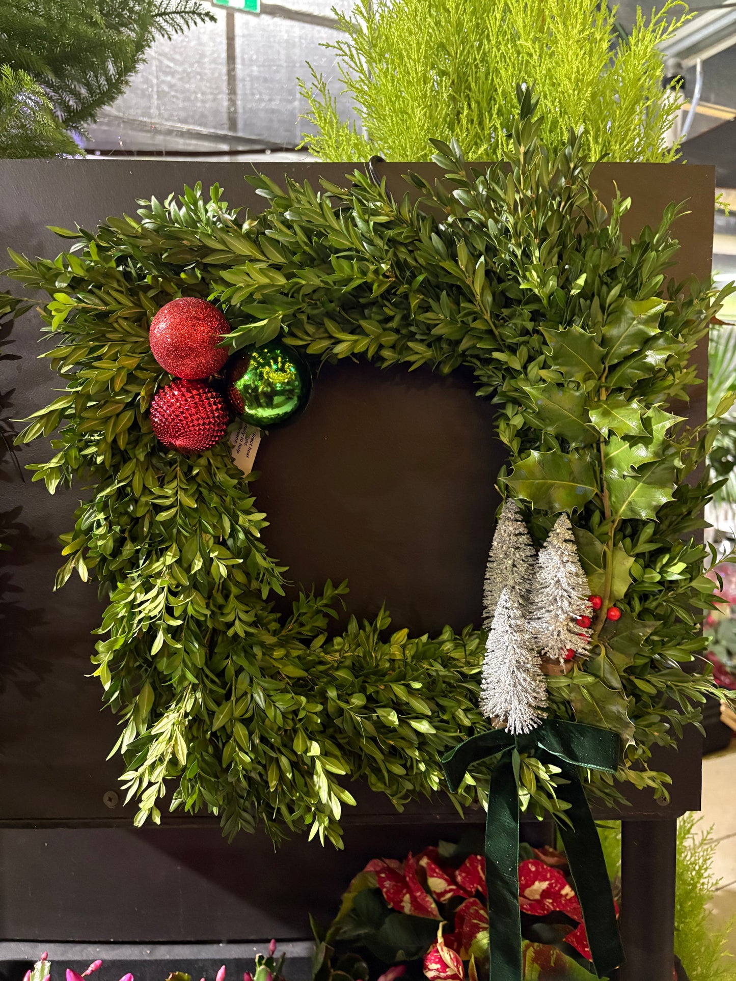 Green specialty live wreath with red ornaments on a dark surface