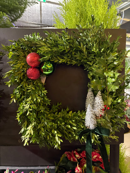 Green specialty live wreath with red ornaments on a dark surface