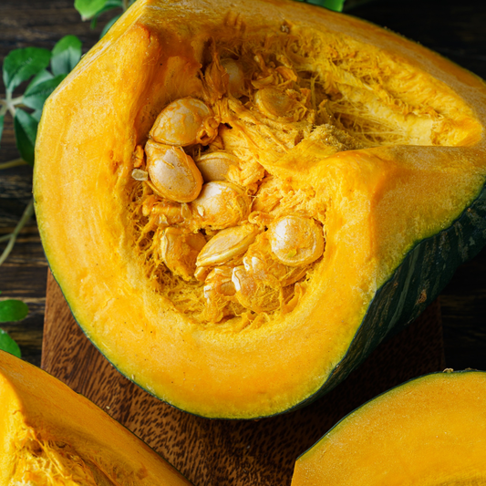a bright orange squash sweet mama kabocha cut open with the innards and seeds visible on a wooden surface