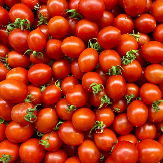 A close-up, top-down view of a dense pile of ripe, red sweet million cherry tomatoes with small green stems visible.